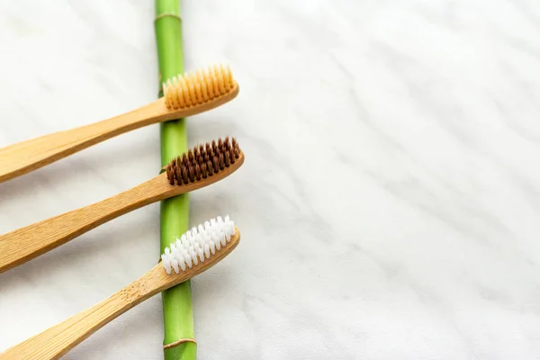 Bamboe tandenborstels, bamboe plant op witte marmeren achtergrond. Plat gelegd. Natuurlijke badproducten.Biologisch afbreekbare natuurlijke bamboe tandenborstel.Milieuvriendelijk, Nul afval, Tandverzorging Kunststof vrij concept — Stockfoto