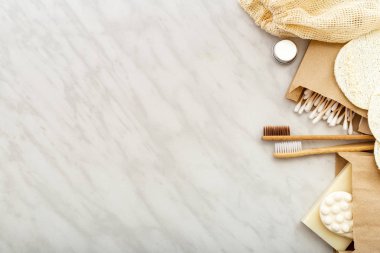 Sıfır atık doğal banyo ürünü. Bambu diş fırçaları, sabun pamuğu çubukları, beyaz mermer zemin üzerindeki lif bezleri. Düz kopya alanı. Çevre dostu, sıfır atık, plastik diş bakımı.