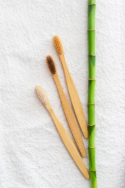 Bambusz fogkefék, bambusz növény fehér törölközőn, márvány háttér. Lapos fekvés. Természetes fürdő termékek.Biológiailag lebomló természetes bambusz fogkefe.Környezetbarát, Zéró hulladék, Fogápolás Műanyagmentes koncepció — Stock Fotó