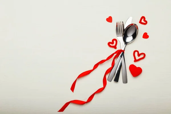Cutlery tired by red ribbon with many red hearts at Valentines Day. Festive table setting on a white wooden table. Dinner meal in restaurant. Valentine Day, love, dating concept, copy space, flat lay — Stock Photo, Image