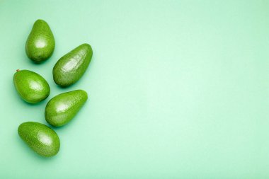 Renkli arka planda taze taze organik yeşil avokadolar, yaz yemekleri konsepti. Nane yeşili arkaplanda minimum düz uzanma stili avokado tüm meyve ve metin için kopyalama alanı.