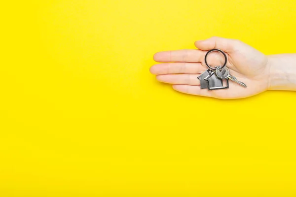 房子钥匙与小饰物在女性手中的色彩背景,顶部视图与复制空间.黄色背景的房子钥匙最小平铺风格，文字位置. — 图库照片
