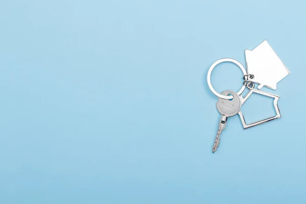 Hus nycklar med prydnad på färg bakgrund, ovanifrån med kopieringsutrymme. Hus nyckel på blå bakgrund. Minimal platt liggstil med plats för text. — Stockfoto