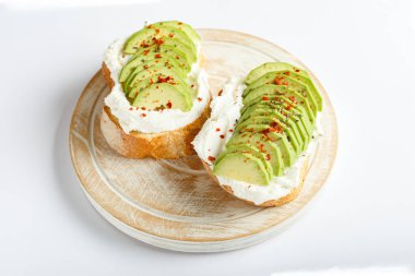 Two avocado toasts, avocado sandwich. Fresh avocado sliced on toast of wheat bread, cream cheese. Avocado sprinkled with chili, basil spices on a white background with place for text, top view.