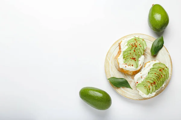 Two avocado toasts, avocados fruit, avocado sandwich. Fresh avocado sliced on toast of wheat bread, cream cheese. Avocado sprinkled with spices on a white background with place for text, top view.