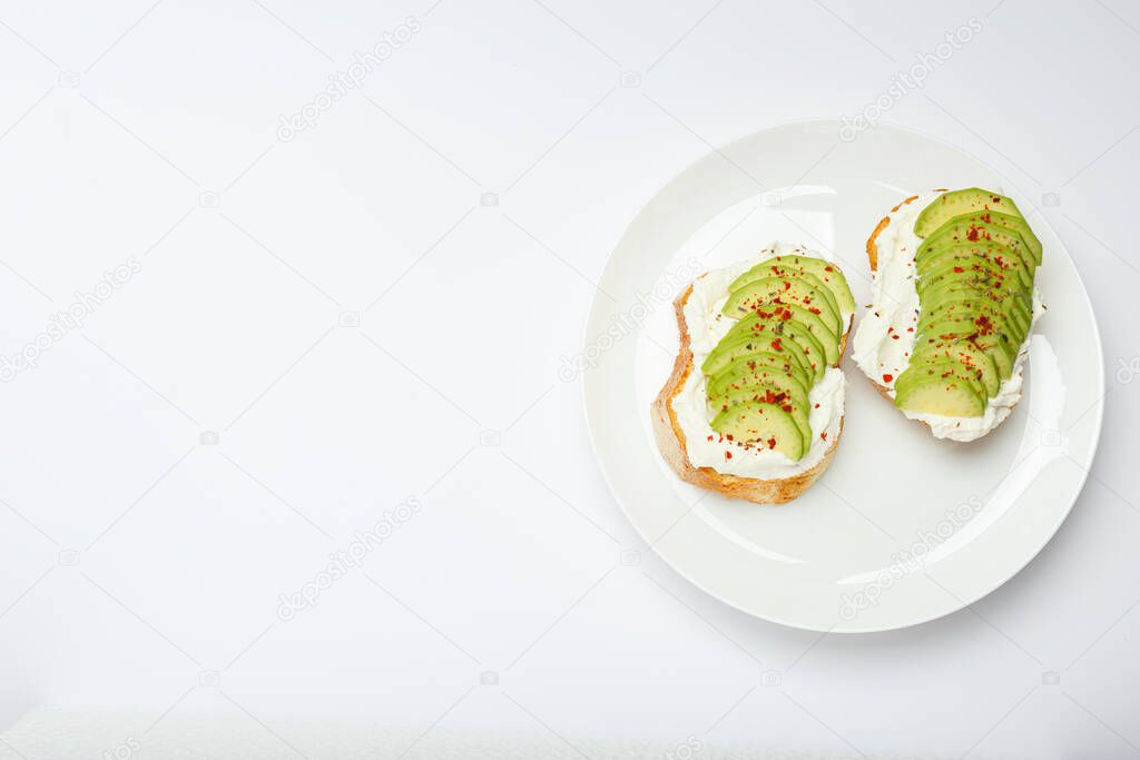 Two avocado toasts, avocado sandwich. Fresh avocado sliced on toast of wheat bread, cream cheese. Avocado sprinkled with chili, basil spices on a white background with place for text, top view.