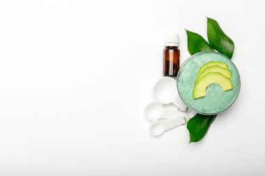Avokado yüz maskesi cam kavanozda, ev yapımı besleyici maske püre, gerekli yağ, kaşıklar. Diy ev yapımı kozmetik tarifi, cilt bakımı. Avokado Düz beyaz arkaplan kopyalama alanı üzerinde yatıyordu