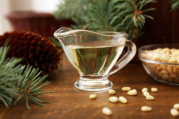 Pine nut oil and bowl of pine nuts on wooden background with cones, cedar brunches.