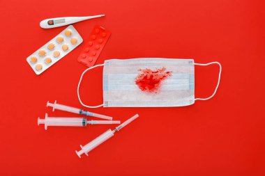 Hemoptisis coronavirus, kırmızı arka planda kan hapları şırıngası termometresi olan koruyucu cerrahi maske. Zatürree, akut solunum enfeksiyonları, tüberküloz, akciğer kanseri, hemofili, salgın..