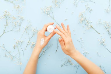 El kremi, kadın eli pastel mavi arka plana organik doğal krem kozmetik uyguluyor. El ve vücut için kavanozda cilt bakım kremi. Yumuşak cilt, sağlık ve güzellik için nemlendirici krem