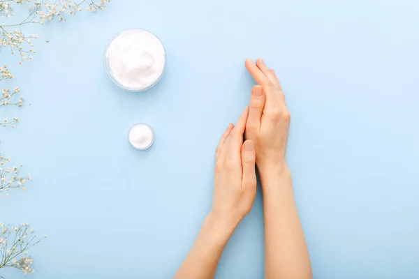 Hand cream, female hands applying organic natural cream cosmetics on a pastel blue colored background. Skin care cream in jar for hands,body. Flat lay moisturizing cream for soft skin, health, beauty