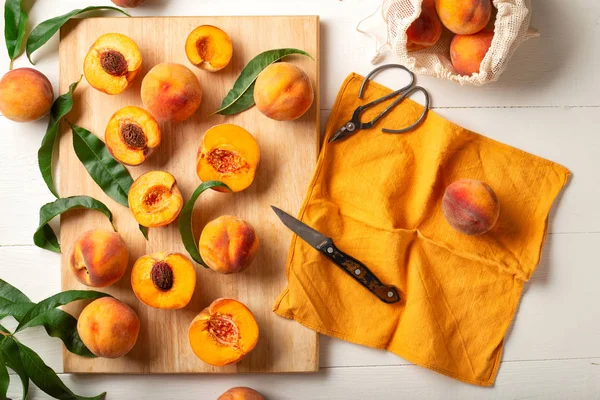 Şeftali, yapraklı bütün meyve, yarı şeftali, beyaz mutfak masasında şeftali dilimleri. Şeftali reçeli yapma, şeftali tatlısı pişirme süreci. Pasta şefi iş yerinde. Düz yatıyordu.