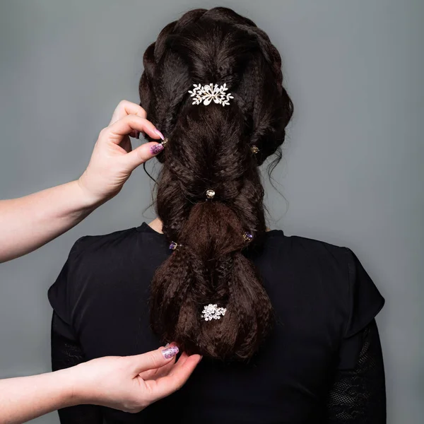 辫子尾毛风格 理发师在灰色背景上为棕色头发的女人做发型 专业美发服务 发型设计工艺 用发夹做辫子 — 图库照片