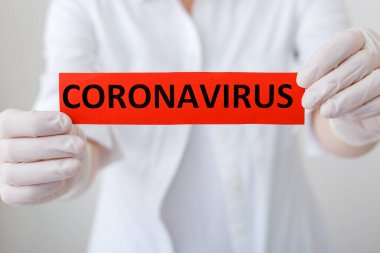 Coronavirus, COVID-19 kırmızı uyarı işareti. Beyaz önlük ve eldivenli doktor ellerinde Coronavirus yazıyor. Karantina koronavirüsü COVID-19 salgını. Coronavirüs salgını gribi