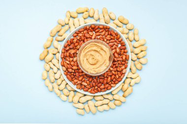 Açık kavanozda fıstıklı krema ezmesi. Fıstık ezmesinin yanında fıstık ezmesi ve soyulmuş fıstık var. Minimalist besin düzlüğü mavi arka planda yatıyordu. Gıda arkaplanı