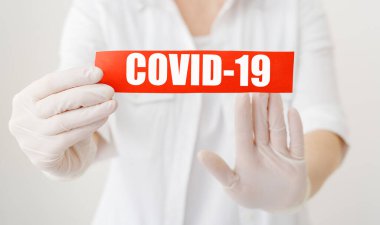 COVID-19 Coronavirus, kırmızı uyarı işareti üzerinde COVID-19 yazılı beyaz önlüklü, eldivenli, yüzü tıbbi maskeli doktor ellerinde. Karantina koronavirüsü salgını. Coronavirus salgını gribi. COVID19.