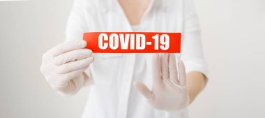 COVID-19 Coronavirus, kırmızı uyarı işareti üzerinde COVID-19 yazılı beyaz önlüklü, eldivenli, yüzü tıbbi maskeli doktor ellerinde. Karantina koronavirüsü salgını. Coronavirus salgını gribi. COVID19.