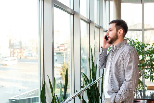 Phone conversation in urban modern office. Smart beard man is negotiating by smartphone. Attractive businessman freelancer in cafe. Young caucasian man holding smartphone for business work