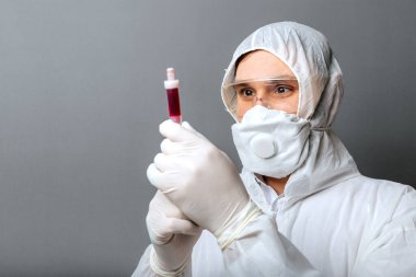 Coronavirus, kovid 19 kan testi doktorların elinde. Koruyucu giysili doktor, biyolojik tehlike, tıbbi maske FFP3, gri arka planda güvenlik gözlükleri. Tıp laboratuarı kavramı.