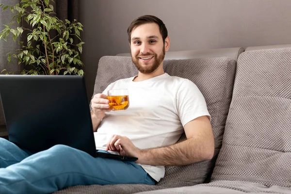 Šťastný Mladý Běloch Pije Čaj Zatímco Pracuje Domova Pomocí Notebooku — Stock fotografie