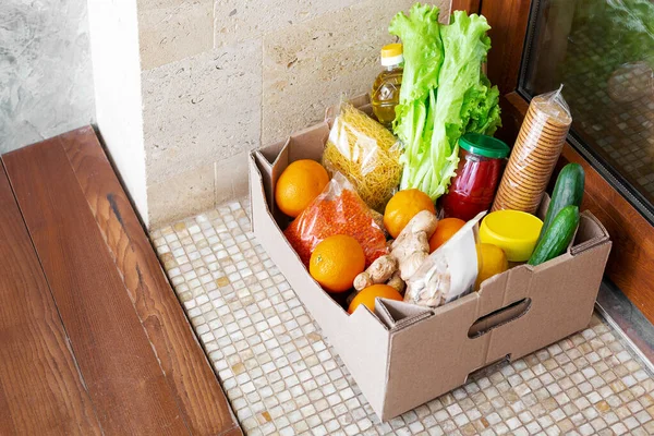 Food delivery or Donation Box during covid quarantine. Contactless social home delivery, safe shopping in coronavirus pandemic. Takeout meal. Food box on doorstep near door. Courier home delivery.