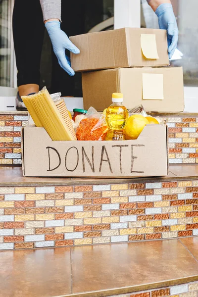 Donation box with food on doorstep near home door. Delivery mail boxes in female hands. Woman in protective gloves holding Delivery donate box,covid 19 quarantine,Self isolation,Stay home,coronavirus.