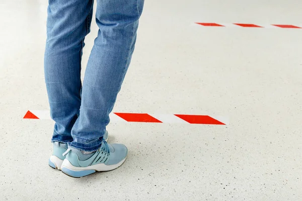 Man stand in line keeping social distance, People standing behind a warning line during covid 19 coronavirus quarantine. Safe shopping, Social distancing concept. Legs in line close up.