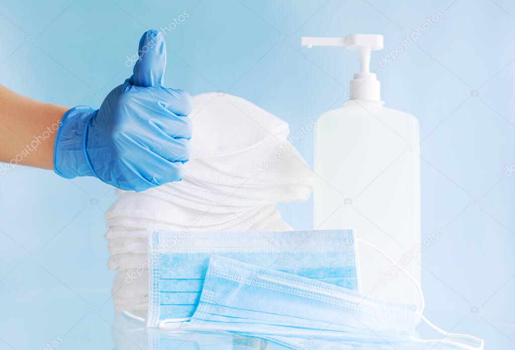 Doctor hand in blue gloves show thumbs up sign. Many different medical face masks, surgical protective disposable mask, alcohol sanitizer gel for hygiene sterility,Coronavirus covid virus prevention.