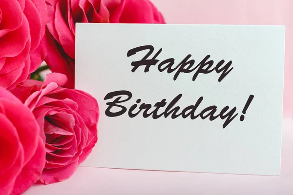 Happy birthday text on card in flower bouquet on pink background. Flower delivery, congratulation card. Greeting card in pink red roses.