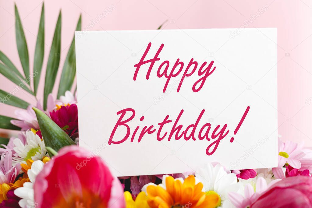 Happy birthday text on card in flower bouquet on pink background. Flower delivery, congratulation card. Greeting card in Tulips, daisies, chrysanthemum