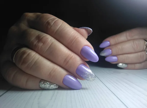 Women\'s manicure on long round nails. Gel lacquer delicate purple color with sequins. Pastel lilac finish with silver flake design