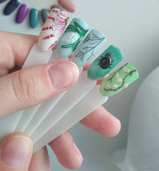 Spring designs on tips. Drawings on manicure tips of green color on the background of a white working manicure table.