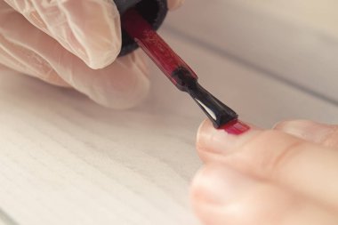 Manikür ustası müşterinin tırnaklarını boyuyor. Fırçalı manikürcü tırnaklarını kırmızıya boyuyor. İlk katman