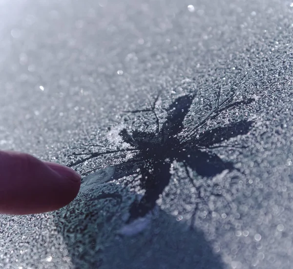 A person draws a snowflake on the frozen glass. Finger painted a beautiful snowflake in the cold.