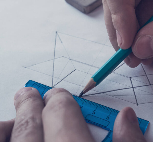 A man draws a diagram with a ruler, eraser and pencil. Design and create a project on a white sheet of paper close-up.