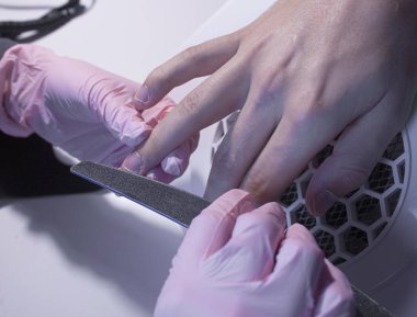 Salonda erkek manikürü. Efendi bir erkek için manikür yapıyor. Manikürcü bir adamın tırnaklarını tırnak törpüsüyle keser. Çivilerin tırnak törpüsüyle hizalanması.