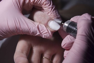 The manicurist removes the coating from the nails with the device. Removing the nail coating with a machine with a cutter. Professional manicure in the salon close-up.