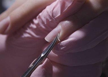 A manicurist cuts off the cuticle of nails with scissors. Cuticle removal with nail scissors. Professional manicure in the salon close-up.