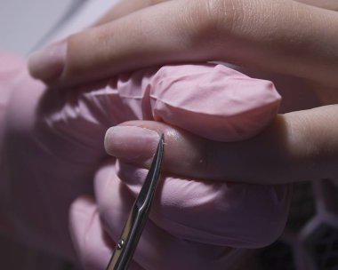 A manicurist cuts off the cuticle of nails with scissors. Cuticle removal with nail scissors. Professional manicure in the salon close-up.