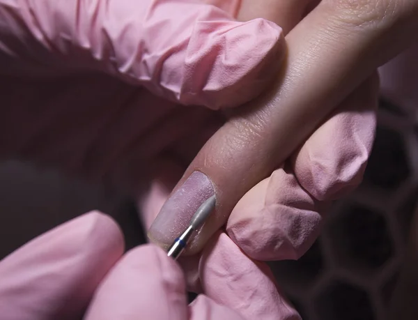 The manicurist cleans the cuticle of the nails with the device. Cuticle removal using a machine with a cutter. Professional manicure in the salon close-up.