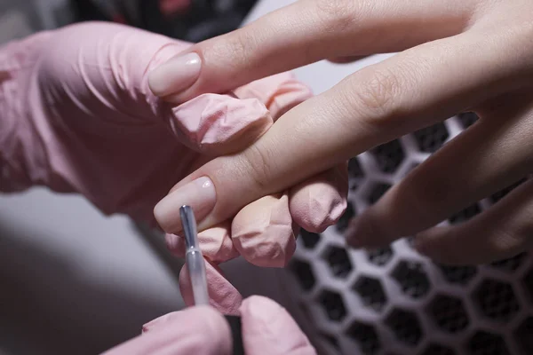 The manicurist applies a layer of gel Polish to the client\'s nail. Applying pink nail Polish with a brush on the background of a vacuum cleaner. Coating the nail plate with nail Polish.