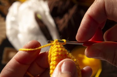Terzi kadın yün örgü örüyor. El işi ve hobiler. Bir örgücü sarı örgü bir oyuncak dikiyor..