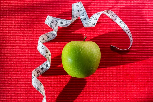 Green apple and Measuring tape on red background. Harsh shadow — Stock Photo, Image