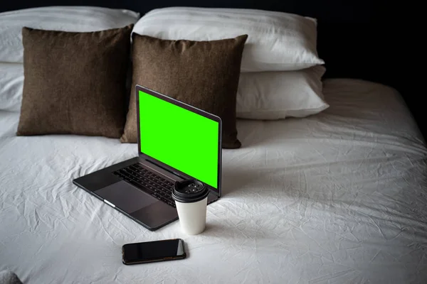 Coffee Cup To Go, Laptop and smartphone on bed. Working from home concept. Green template on screen.