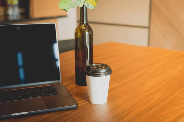 Laptop and cup of take away coffee on a table. Lifestyle concept. Mockup for coffee brand. Green template on laptop