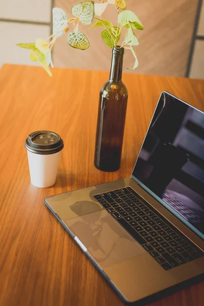 Laptop and cup of take away coffee on a table. Lifestyle concept. Mockup for coffee brand. Green template on laptop
