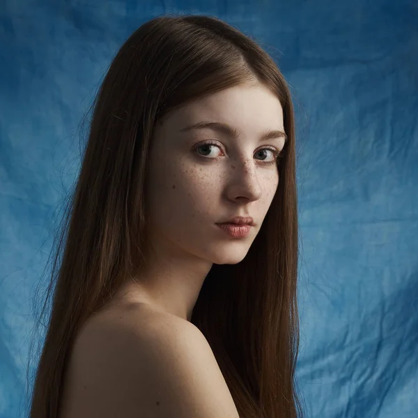 Beauty theme: portrait of a beautiful young girl with freckles on her face and wearing a black dress on a blue background in studio — Stock Photo, Image