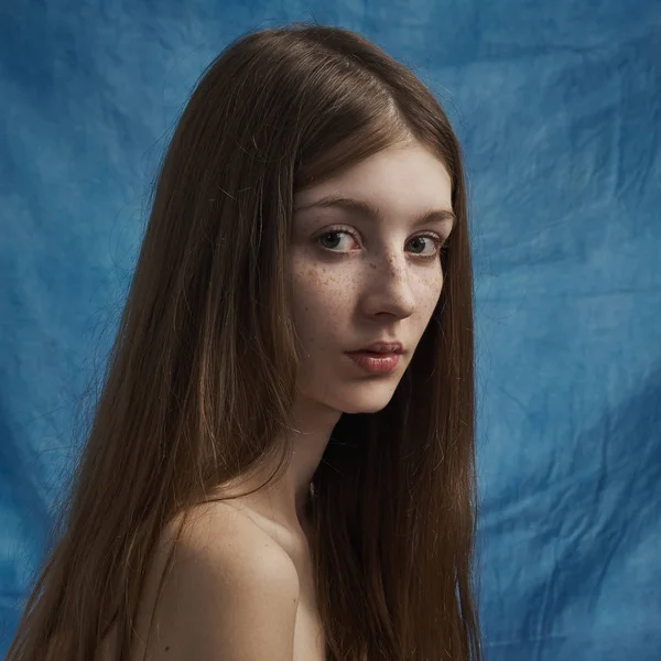 Ομορφιά θέμα: πορτρέτο του μια όμορφη νεαρή κοπέλα με φακίδες στο πρόσωπό της και φορώντας ένα μαύρο φόρεμα σε ένα μπλε φόντο στο studio — Φωτογραφία Αρχείου