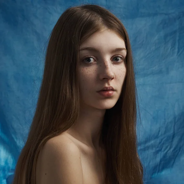 Ομορφιά θέμα: πορτρέτο του μια όμορφη νεαρή κοπέλα με φακίδες στο πρόσωπό της και φορώντας ένα μαύρο φόρεμα σε ένα μπλε φόντο στο studio — Φωτογραφία Αρχείου
