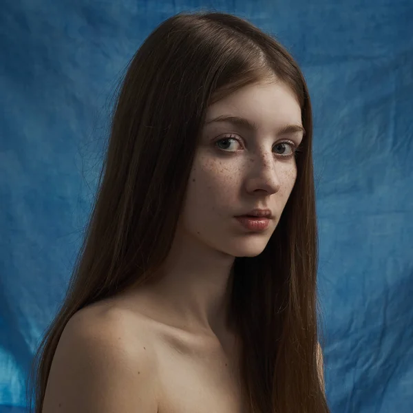 Beauty theme: portrait of a beautiful young girl with freckles on her face and wearing a black dress on a blue background in studio — Stock Photo, Image